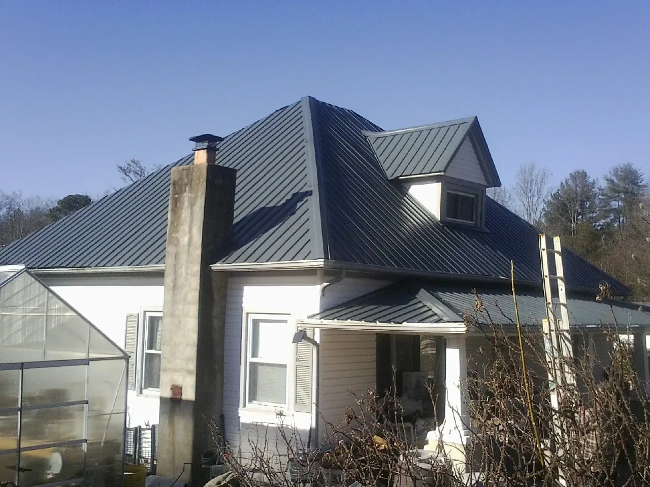 Dark blue standing seam metal roof on a white farmhouse with dormer — Slate & Tile Roof Repair by Roofing Brothers in Delcambre