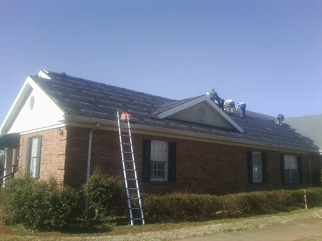 Crew tearing shingles off a brick ranch roof with a ladder set — Emergency Roof Repair work by our crew in Delcambre