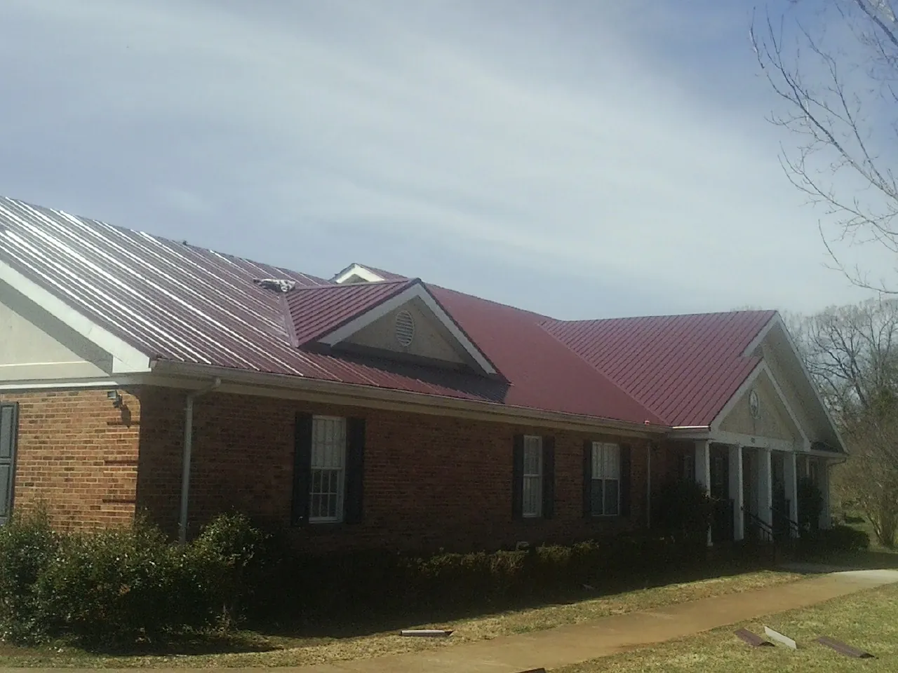 Red metal roof with gabled entries on a long brick building, from a Hail Damage Roof Repair job in Delcambre