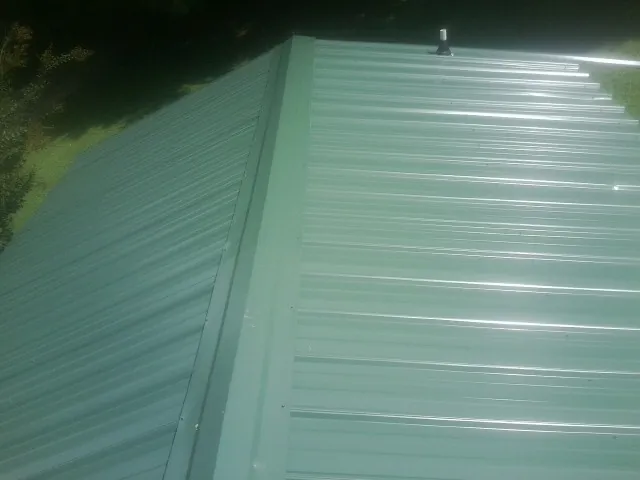 New green metal panels meeting at the ridge of a roof — Flat Roof Repair work by our crew in Delcambre