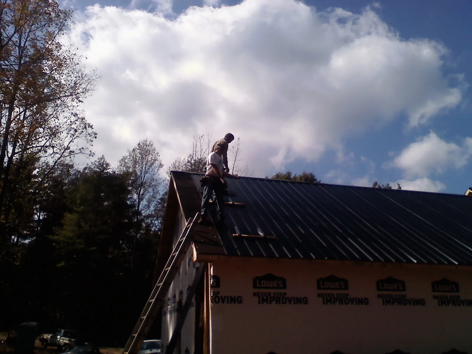 Roofer fastening dark metal panels high against a cloudy sky, from a Roof Inspection job in Delcambre