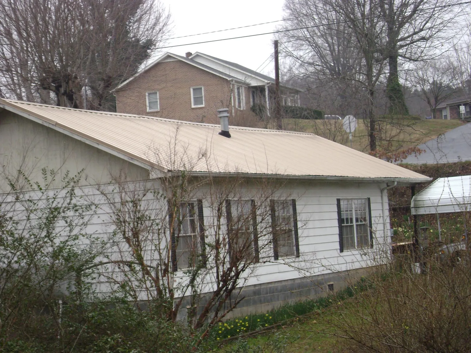 Tan metal roof on a white sided house set into a hillside — Commercial Roofing by Roofing Brothers in Delcambre